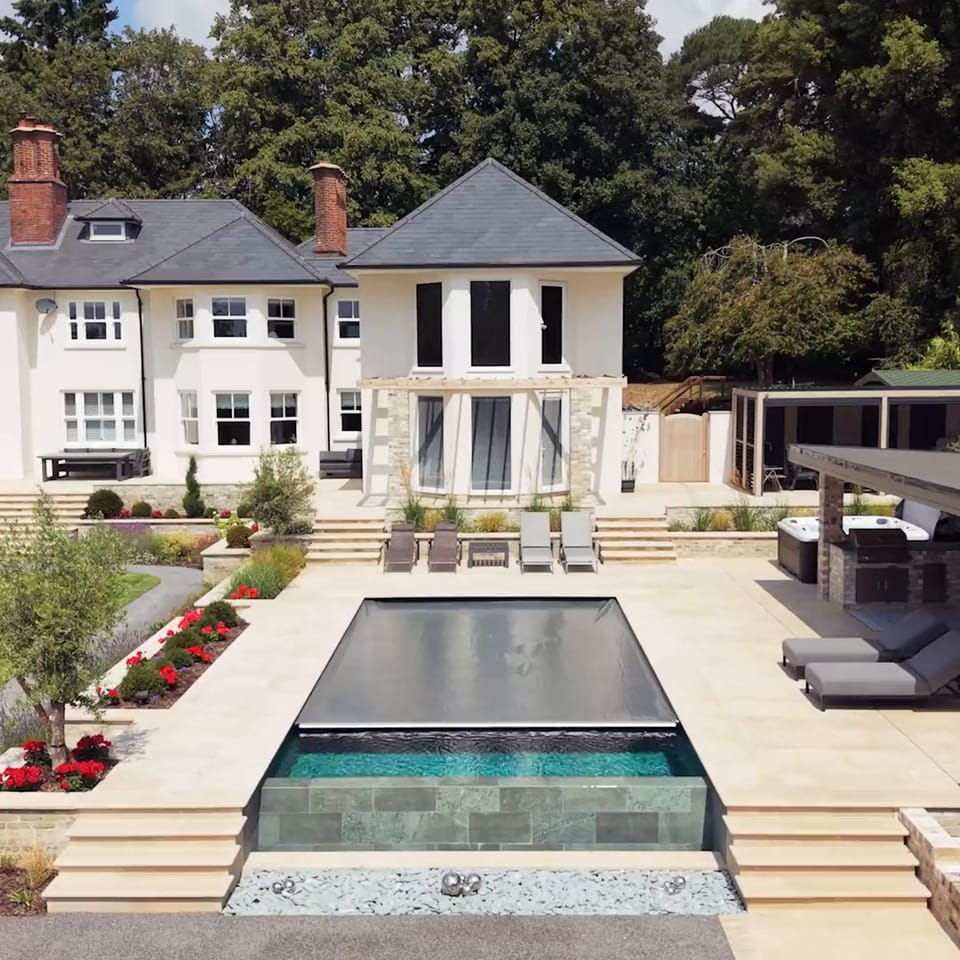 Aerial view of a bespoke outdoor swimming pool beside a country house at Nateley Scures